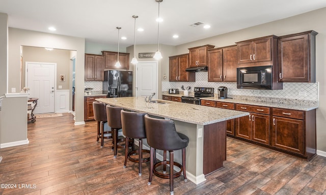 kitchen featuring a kitchen breakfast bar, hanging light fixtures, black appliances, light stone countertops, and a center island with sink