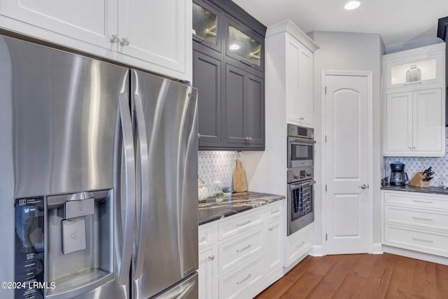 kitchen with dark wood-type flooring, tasteful backsplash, appliances with stainless steel finishes, dark stone counters, and white cabinets