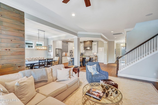 living room featuring ceiling fan with notable chandelier, light hardwood / wood-style flooring, and ornamental molding