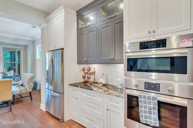 kitchen featuring crown molding, light hardwood / wood-style flooring, white cabinetry, stainless steel appliances, and decorative backsplash