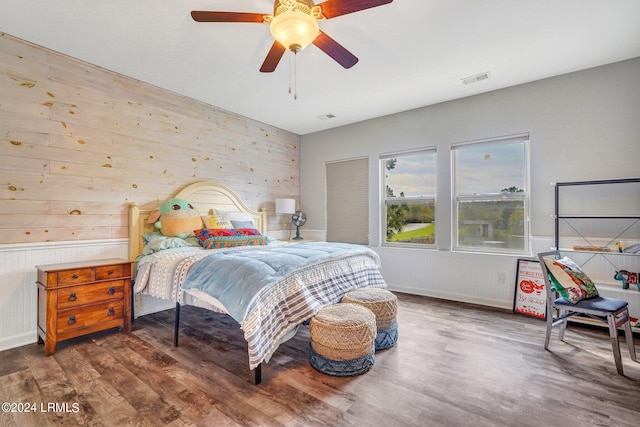 bedroom with dark hardwood / wood-style floors, ceiling fan, and wood walls