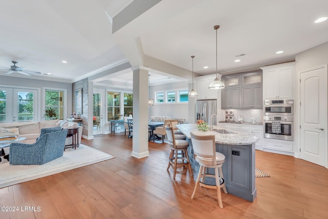 kitchen featuring appliances with stainless steel finishes, sink, hanging light fixtures, light stone counters, and a center island with sink