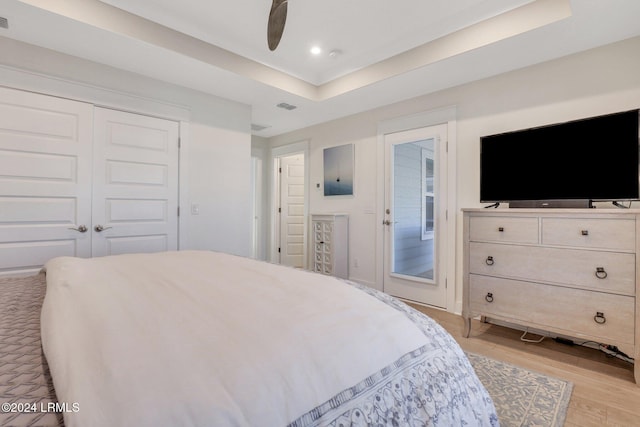 bedroom with ceiling fan, a tray ceiling, light hardwood / wood-style floors, and a closet