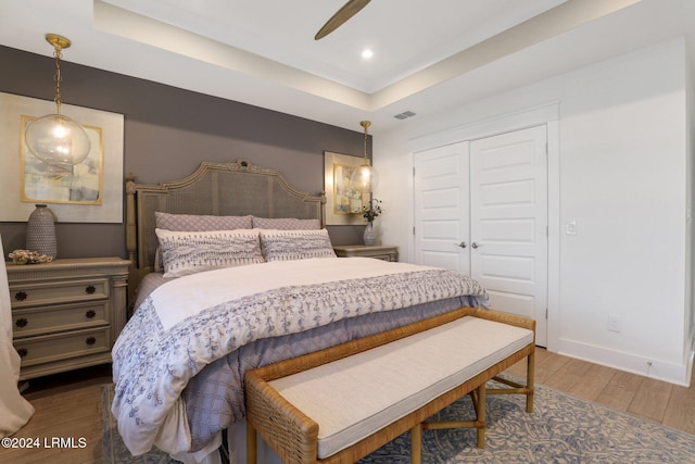 bedroom featuring a raised ceiling, wood-type flooring, ceiling fan, and a closet