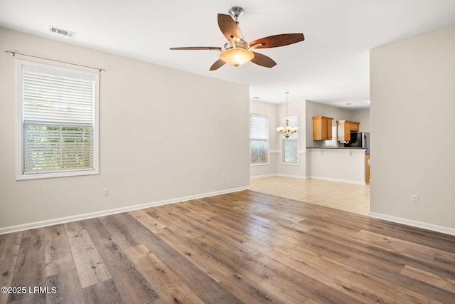 unfurnished living room featuring baseboards, visible vents, light wood finished floors, and ceiling fan with notable chandelier