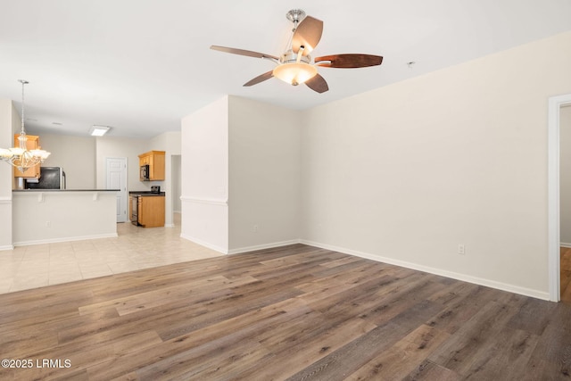unfurnished living room featuring baseboards, light wood finished floors, and ceiling fan with notable chandelier