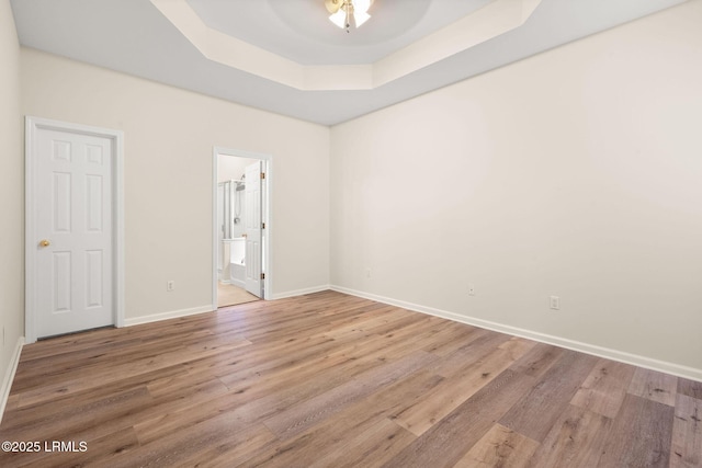 unfurnished bedroom featuring baseboards, connected bathroom, wood finished floors, and a tray ceiling
