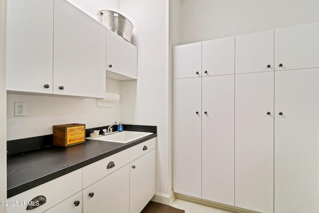 kitchen featuring dark countertops, white cabinetry, and a sink