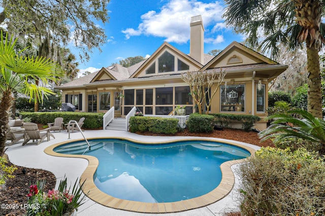 rear view of house with a patio, an outdoor pool, a sunroom, stucco siding, and a chimney