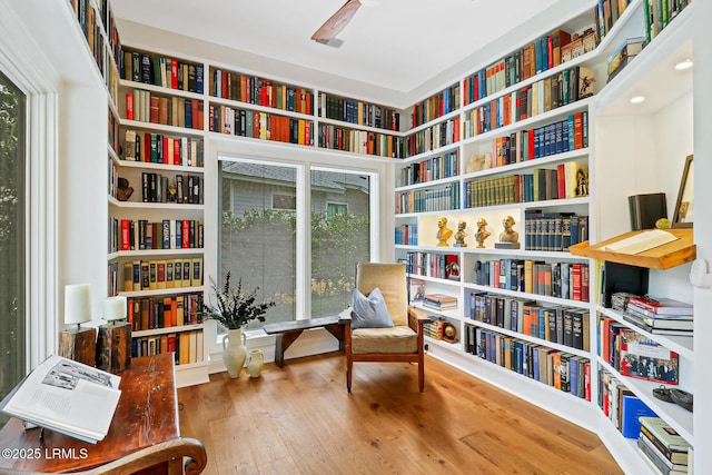 sitting room featuring wall of books, ceiling fan, and wood finished floors