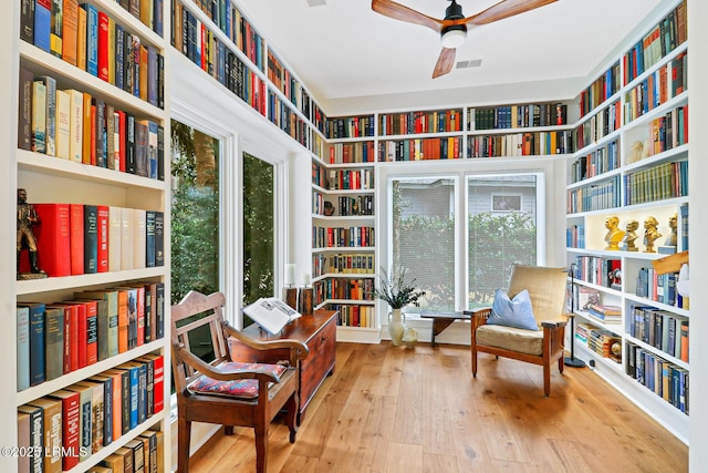 sitting room featuring a ceiling fan, bookshelves, visible vents, and wood finished floors