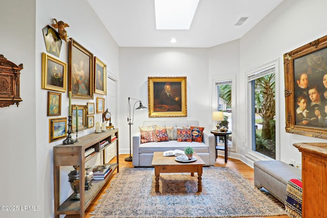 living room featuring light wood-style floors, a skylight, visible vents, and baseboards