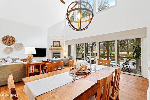 dining room with high vaulted ceiling, plenty of natural light, a glass covered fireplace, and light wood-style flooring