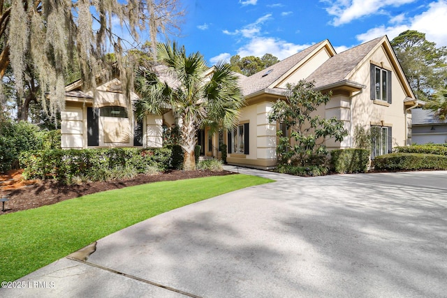 view of front facade with a shingled roof, a front yard, and stucco siding