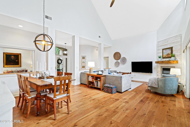 dining space with light wood finished floors, baseboards, visible vents, a fireplace, and high vaulted ceiling