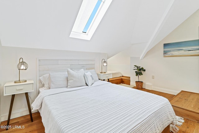 bedroom featuring vaulted ceiling with skylight, baseboards, and wood finished floors