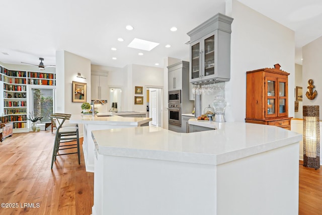 kitchen featuring glass insert cabinets, light countertops, appliances with stainless steel finishes, and a kitchen bar