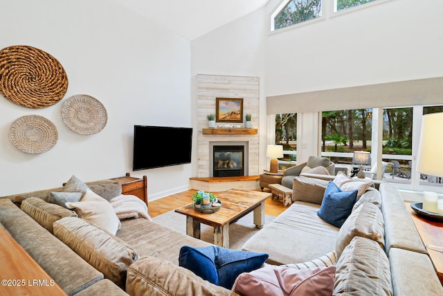 living room featuring light wood-style floors, a glass covered fireplace, high vaulted ceiling, and baseboards