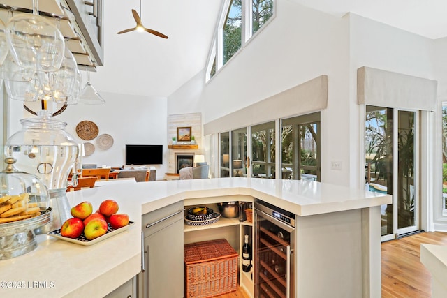 kitchen with wine cooler, light countertops, a towering ceiling, light wood-style floors, and open floor plan