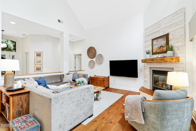 living room featuring high vaulted ceiling, a fireplace, wood finished floors, visible vents, and baseboards