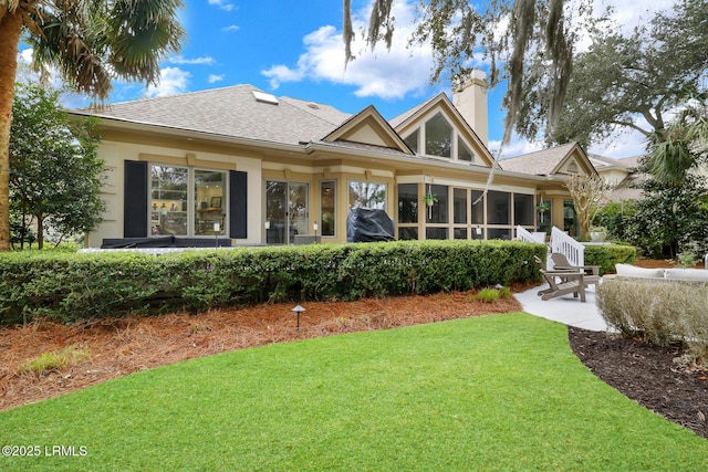 rear view of property with a shingled roof, a sunroom, a lawn, stucco siding, and a chimney