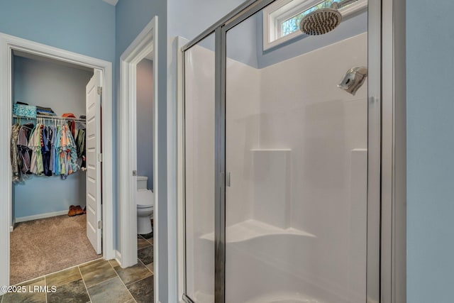 bathroom featuring a shower stall, a spacious closet, toilet, and baseboards