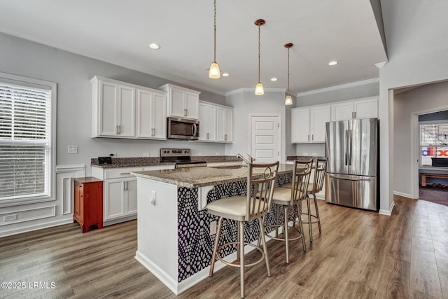 kitchen featuring a kitchen bar, a kitchen island with sink, wood finished floors, stainless steel appliances, and white cabinets