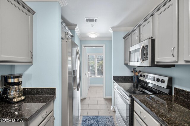 kitchen featuring light tile patterned floors, crown molding, gray cabinets, appliances with stainless steel finishes, and dark stone countertops