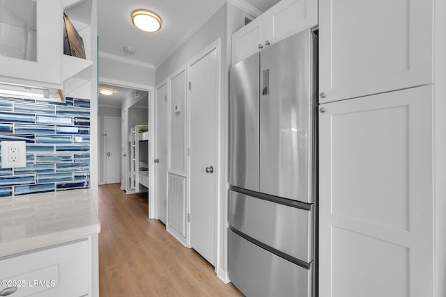 kitchen featuring stainless steel refrigerator, white cabinets, light stone counters, light hardwood / wood-style floors, and crown molding