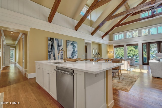 kitchen featuring white cabinetry, light stone countertops, an island with sink, and light wood-type flooring