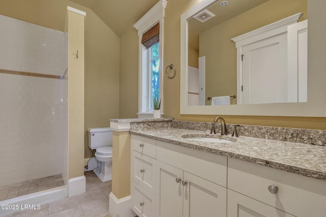 bathroom featuring vanity, a tile shower, vaulted ceiling, tile patterned floors, and toilet