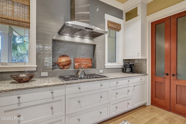 kitchen featuring light stone countertops, stainless steel gas cooktop, white cabinets, wall chimney exhaust hood, and light wood-type flooring