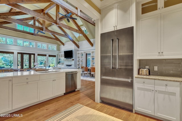 kitchen featuring appliances with stainless steel finishes, white cabinets, decorative backsplash, light stone countertops, and light hardwood / wood-style flooring