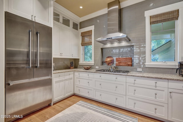 kitchen with appliances with stainless steel finishes, white cabinetry, light hardwood / wood-style floors, light stone counters, and wall chimney exhaust hood