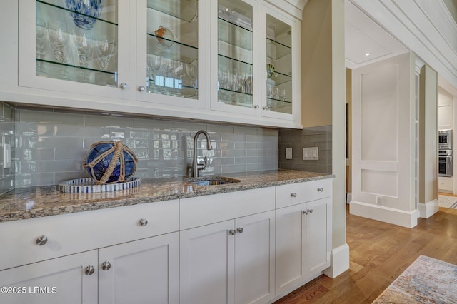 bar with white cabinetry, sink, light stone counters, and light wood-type flooring