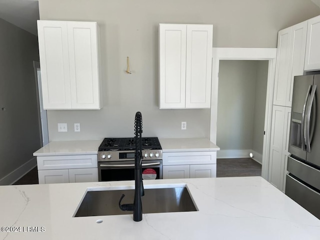 kitchen with light stone countertops, stainless steel appliances, sink, and white cabinets