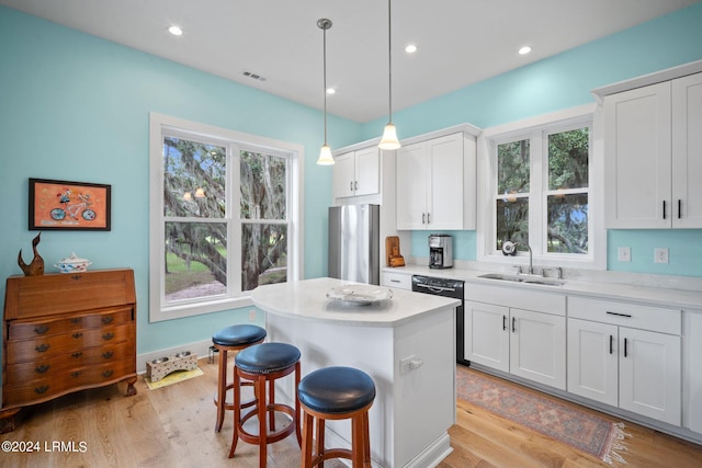 kitchen featuring stainless steel refrigerator, white cabinetry, sink, and pendant lighting