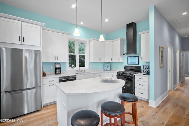 kitchen with decorative light fixtures, white cabinets, a center island, black appliances, and wall chimney range hood