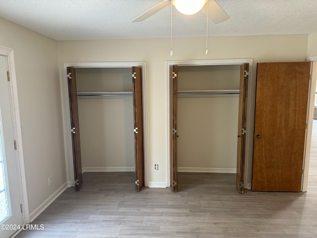 unfurnished bedroom featuring two closets, a textured ceiling, ceiling fan, and light wood-type flooring