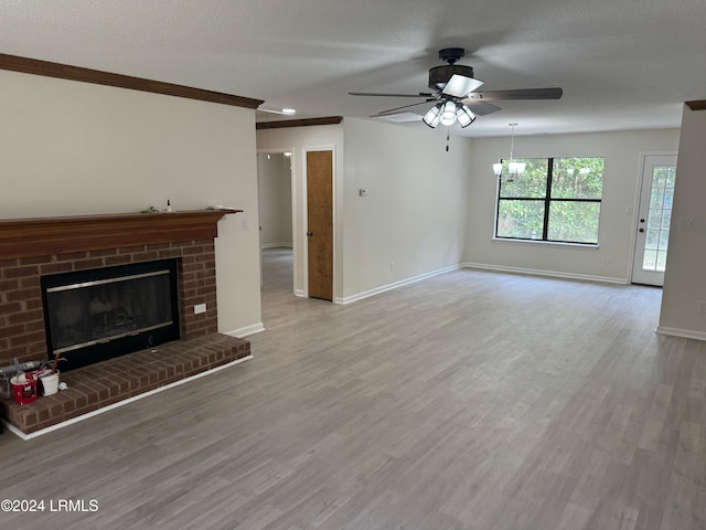 unfurnished living room featuring a brick fireplace, ceiling fan with notable chandelier, light hardwood / wood-style flooring, and a textured ceiling