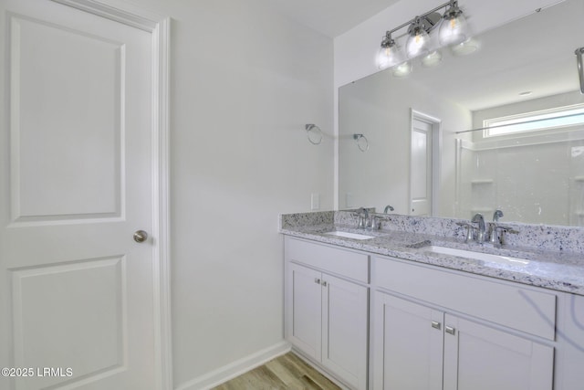 bathroom with double vanity, baseboards, a sink, and wood finished floors