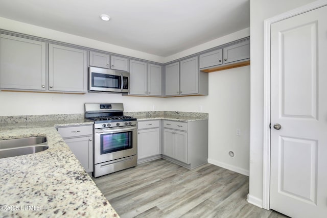 kitchen featuring baseboards, light stone countertops, gray cabinets, stainless steel appliances, and light wood-type flooring