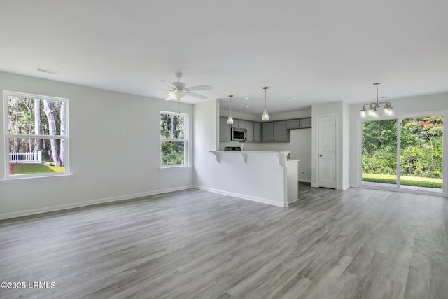 unfurnished living room featuring ceiling fan with notable chandelier, recessed lighting, light wood-type flooring, and baseboards