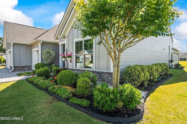 view of side of home featuring stone siding, a garage, a lawn, a shingled roof, and board and batten siding