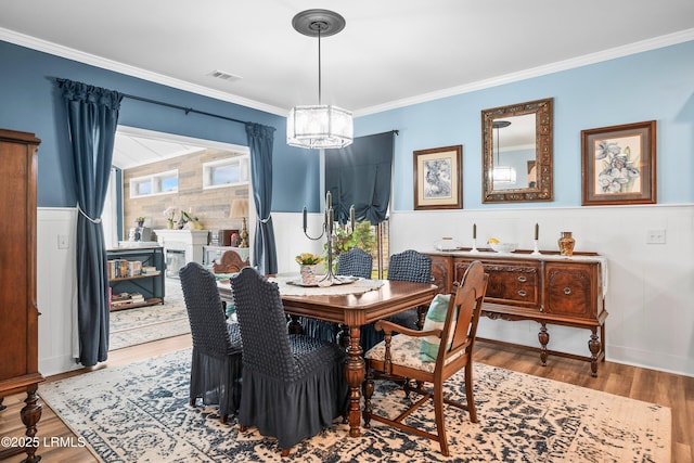 dining area with ornamental molding, wainscoting, visible vents, and wood finished floors