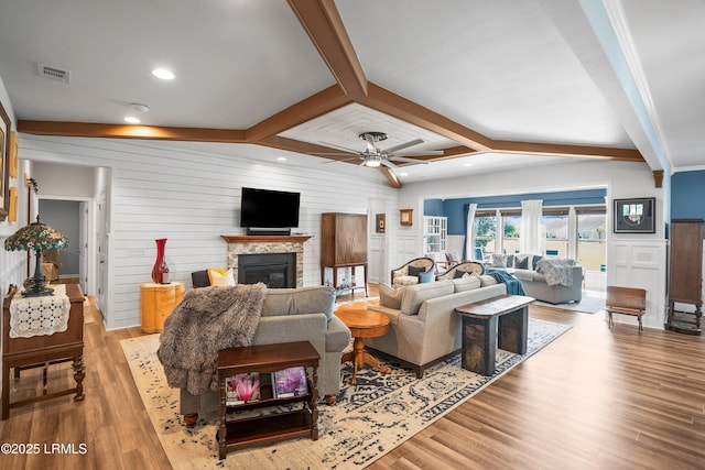 living area featuring light wood finished floors, visible vents, beamed ceiling, and a glass covered fireplace
