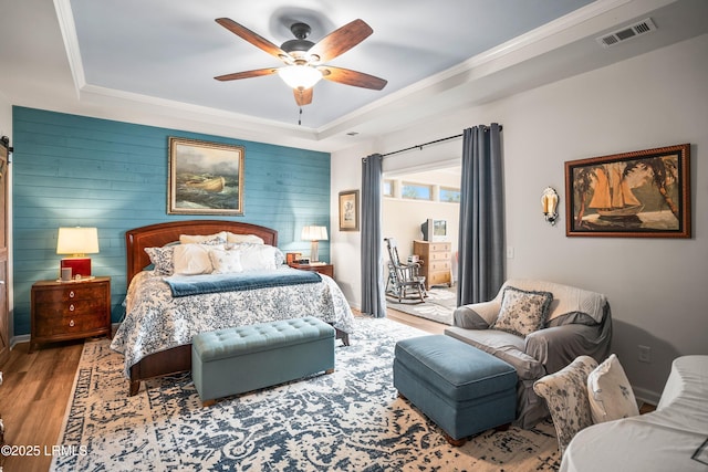 bedroom featuring a tray ceiling, visible vents, crown molding, wood finished floors, and access to exterior