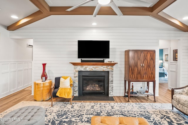 living room featuring a fireplace with flush hearth, beamed ceiling, a ceiling fan, and wood finished floors