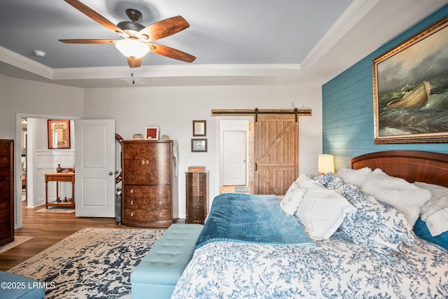 bedroom with a tray ceiling, a barn door, ornamental molding, ceiling fan, and wood finished floors