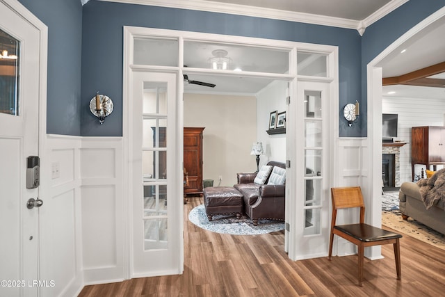 interior space featuring wainscoting, ornamental molding, a fireplace with raised hearth, and wood finished floors